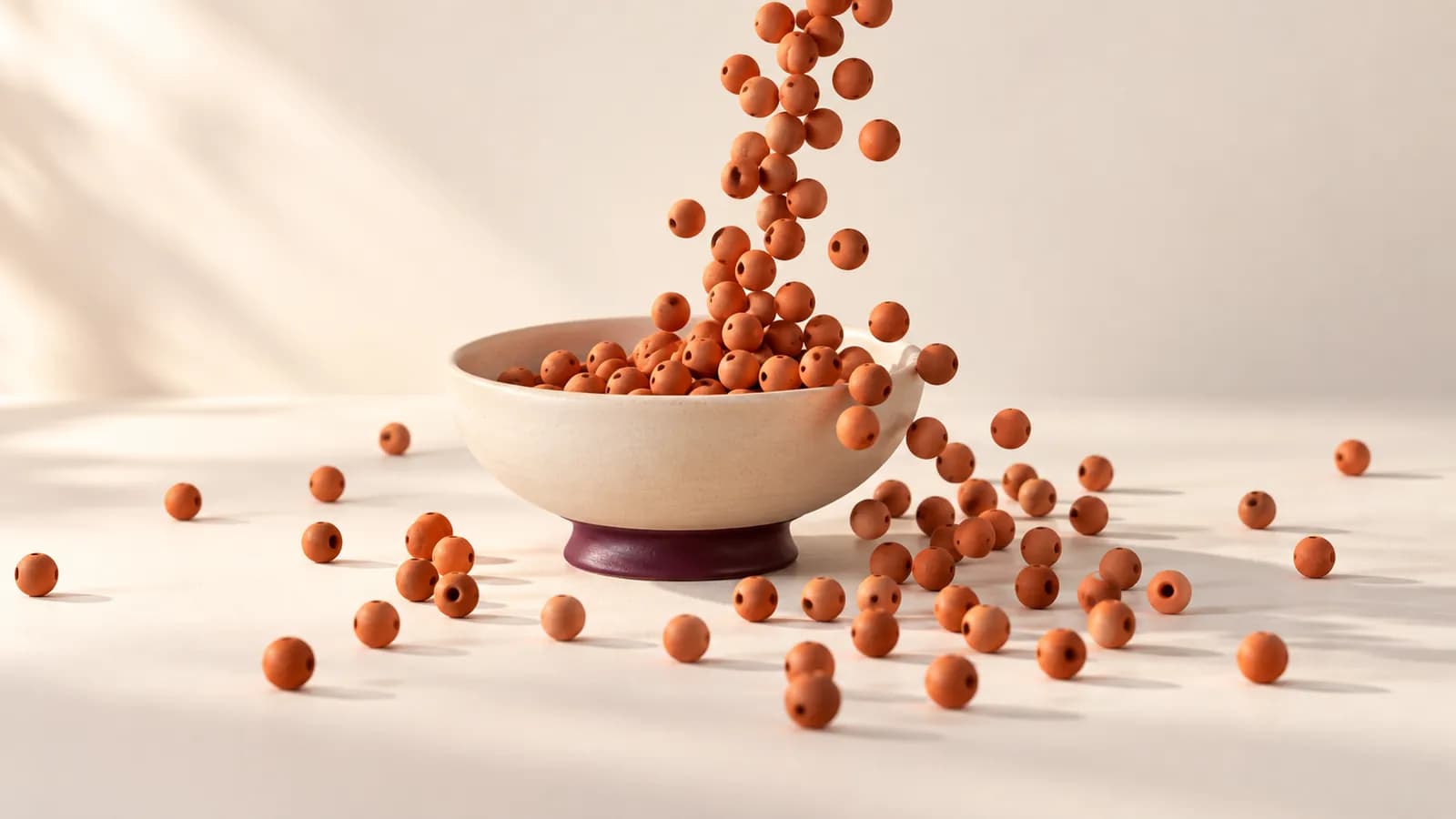 A small ceramic dish overflowing as terracotta beads pour in and scatter across the table