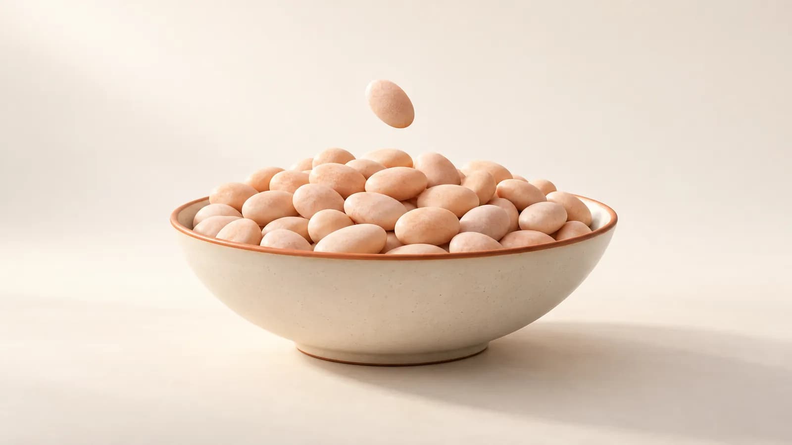 A bowl of identical peach pebbles with one more identical pebble dropping in