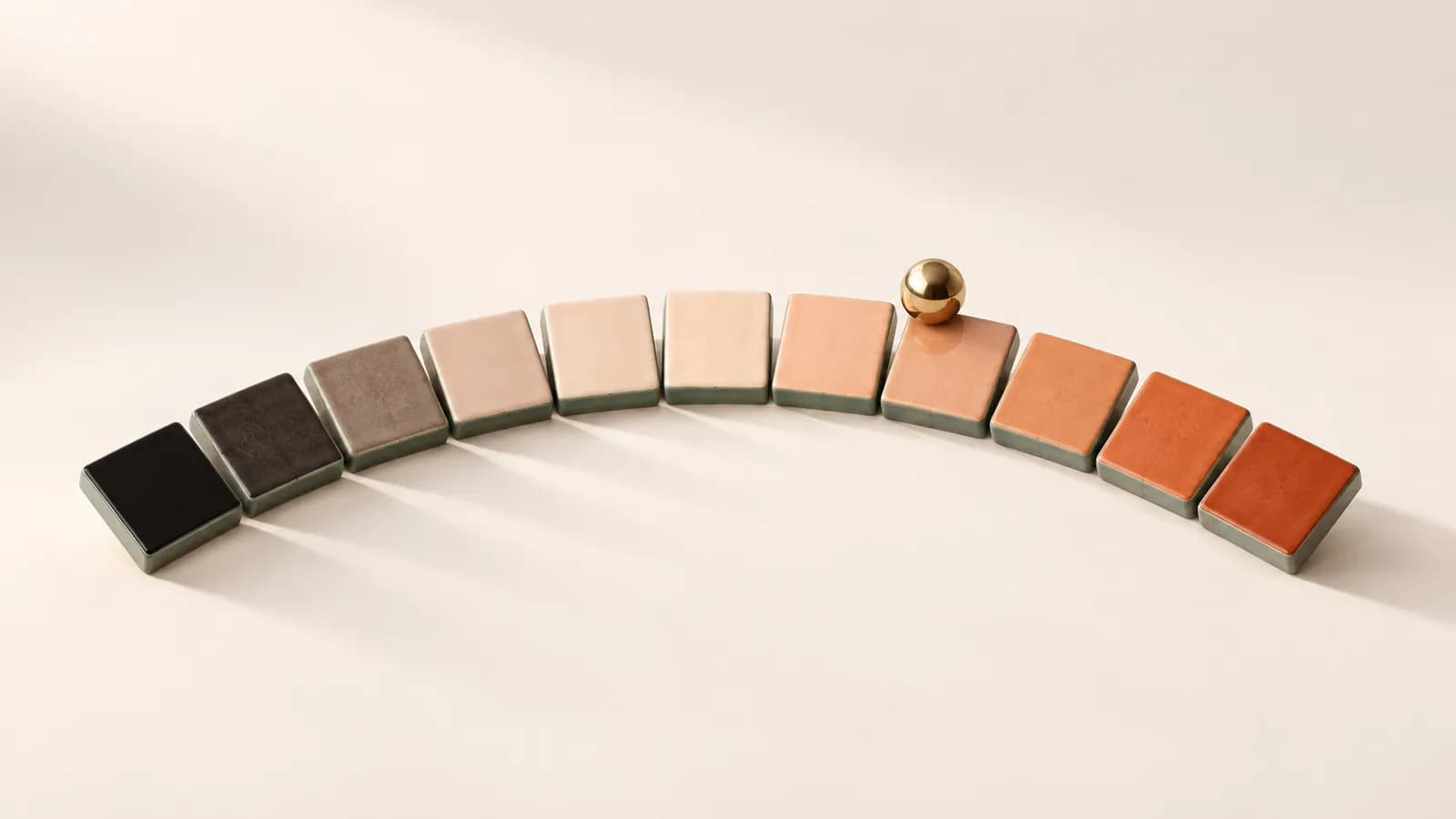 An arc of eleven ceramic tiles shading from black to terracotta, with a brass marble on a high tile