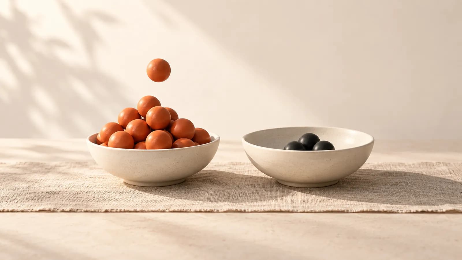 Two ceramic bowls of marbles, one heaped with terracotta marbles and a marble dropping into it