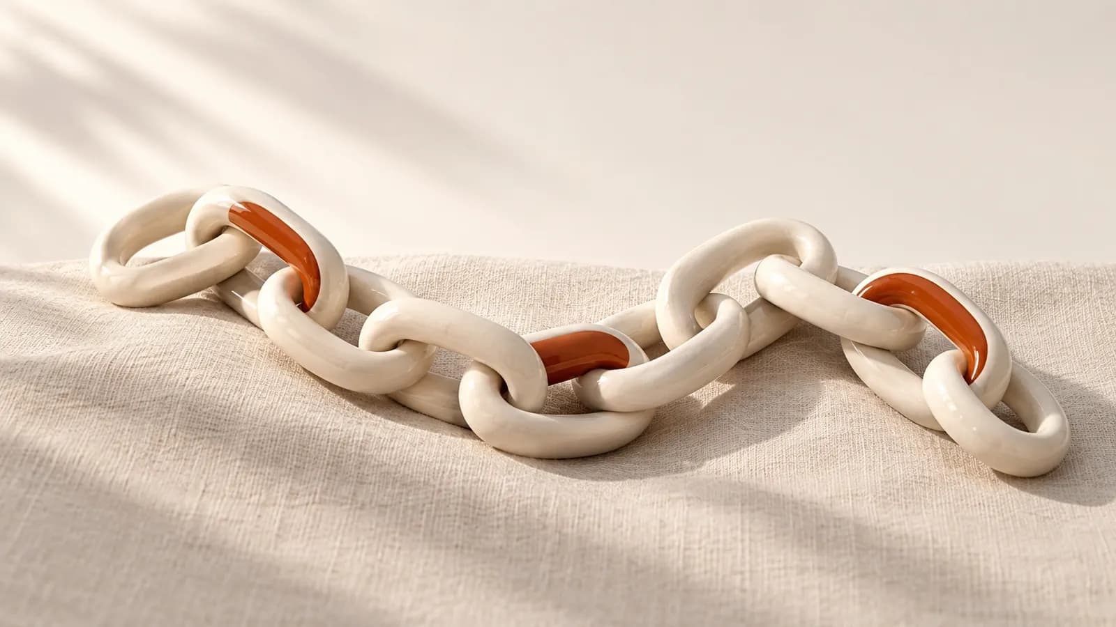 A chain of ceramic links on linen, with some links already filled with terracotta inlay